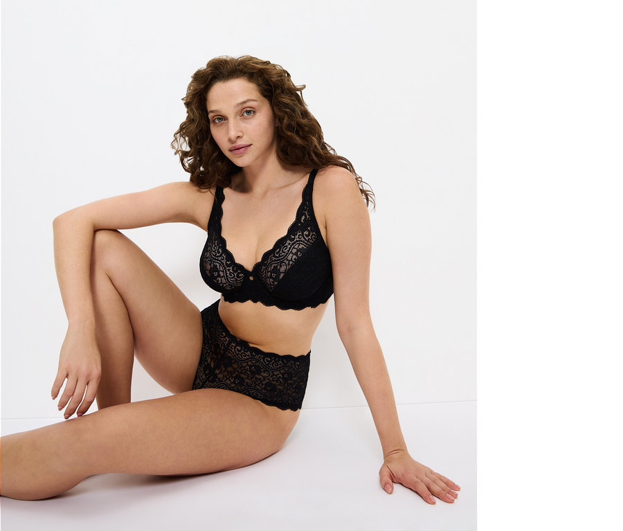 Kobieta siedzi na podłodze w czarnym koronkowym biustonoszu i majtkach.