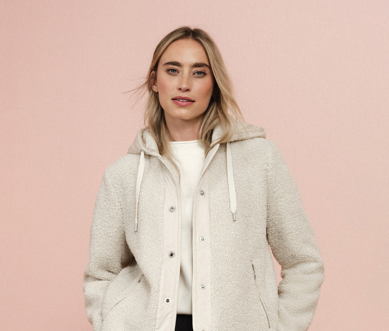 Kobieta ma na sobie bluzę pluszową z odpinanym kapturem Street One na różowym tle.