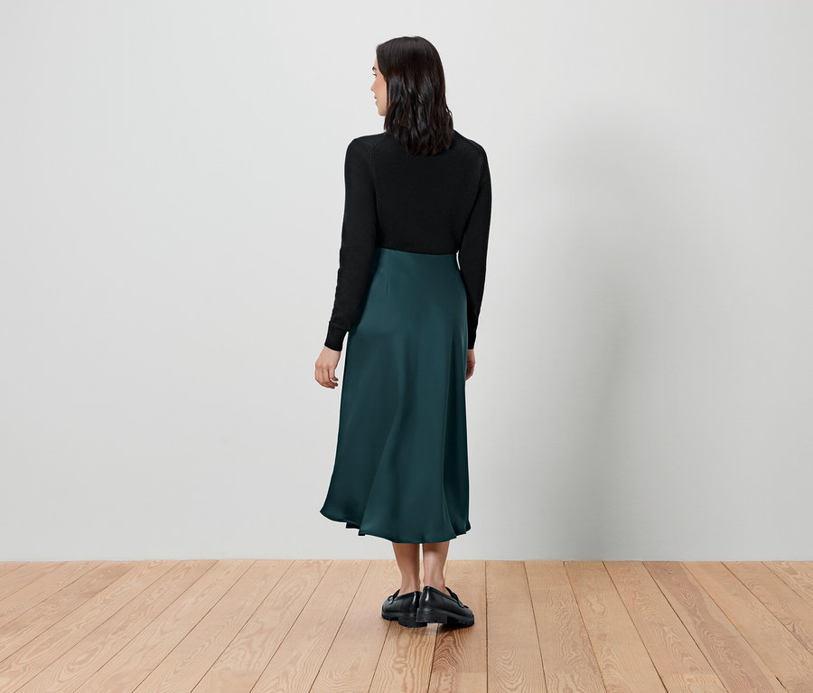 Kobieta stoi tyłem, ubrana w czarny top i zieloną spódnicę.