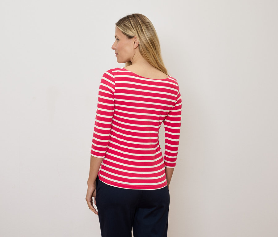 Blondynka patrzy w lewo, ubrana w czerwono-białą bluzkę w paski z rękawami 3/4.
