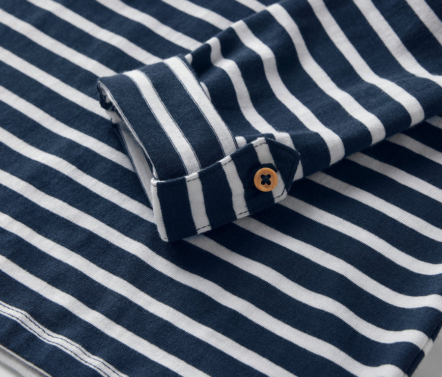 Zbliżenie na detal dziecięcej koszulki z długim rękawem w niebiesko-białe paski z guzikiem.