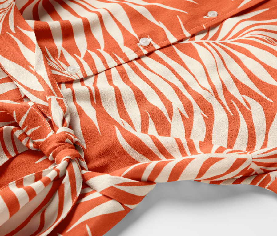 Detale wzorzystej sukienki koszulowej z guzikami i wiązaniem w pasie.