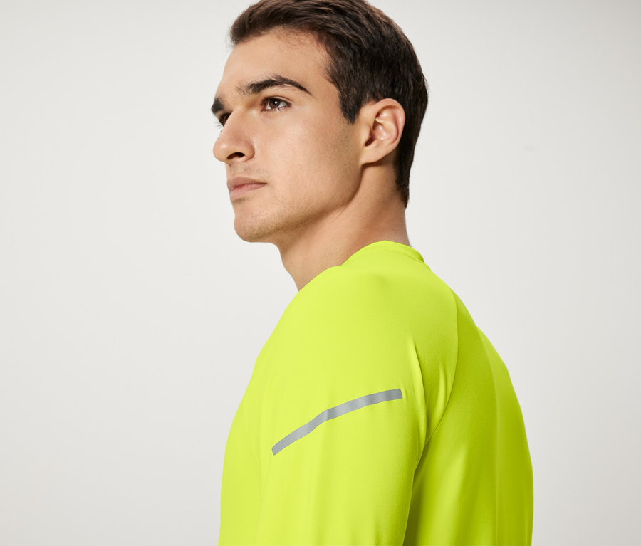 Mężczyzna z brązowymi włosami w neonowożółtej koszulce patrzy w lewo.