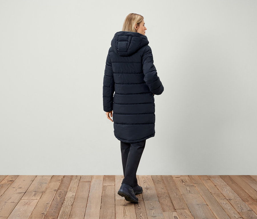 Kobieta w granatowej kurtce puchowej z kapturem, tyłem do aparatu.