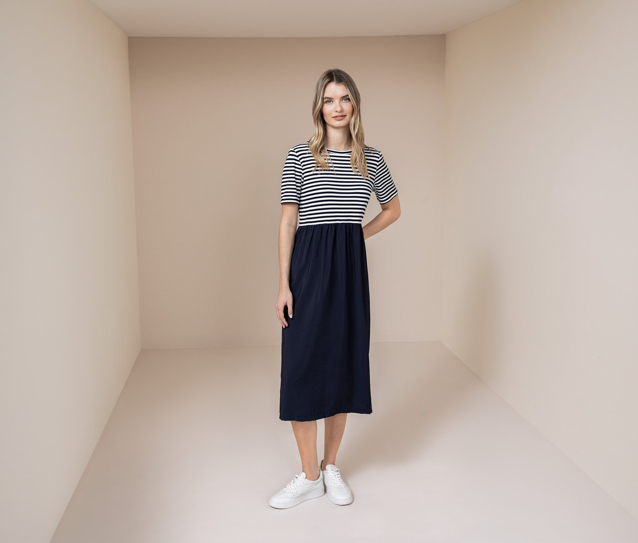 Kobieta w sukience Street One z biało-granatową górą w paski i granatowym dołem oraz białych sneakersach.