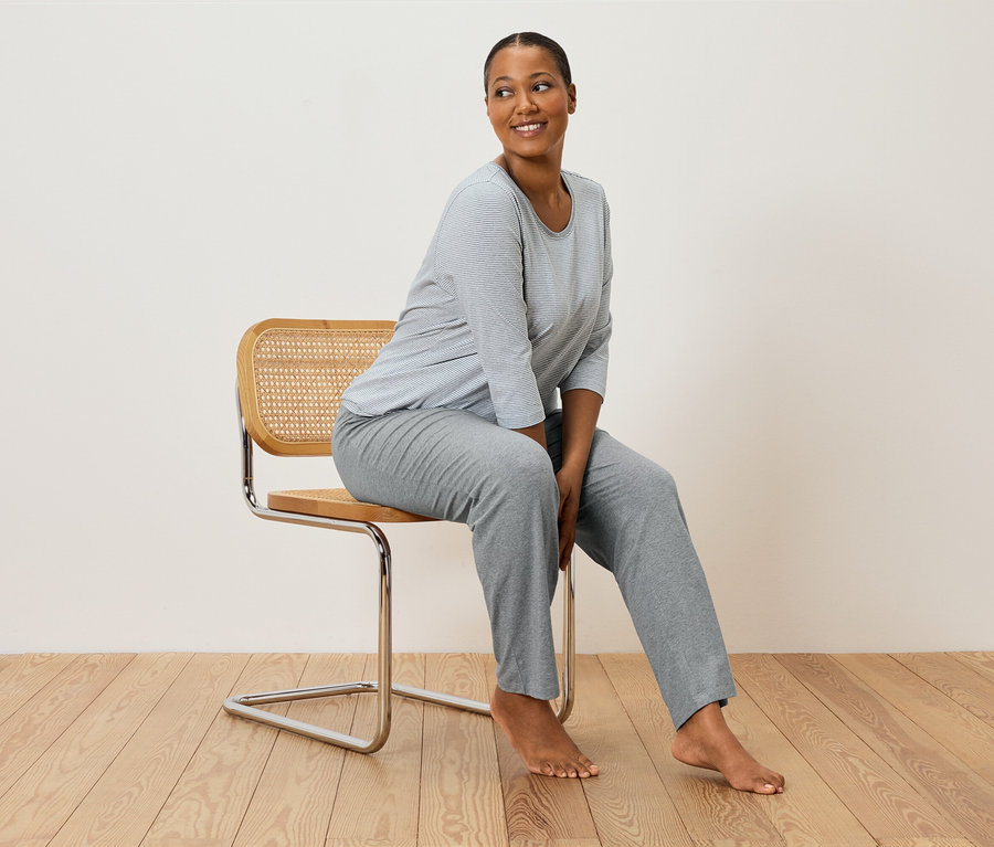 Kobieta siedzi na krześle w szarym piżamie w paski.