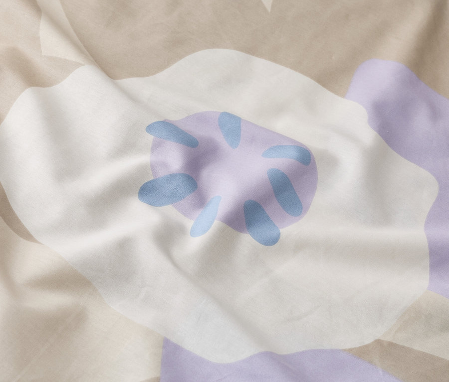 Zbliżenie na pomiętą pościel z dużym kwiatowym wzorem w kolorze białym, fioletowym i beżowym.