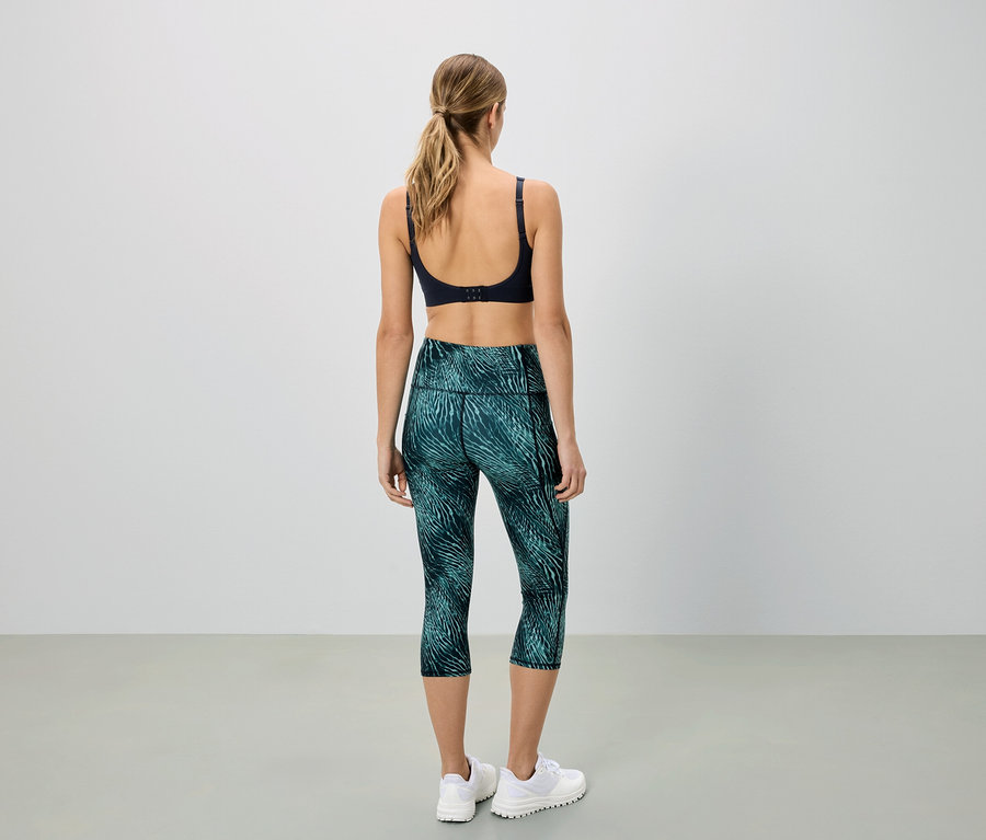 Kobieta widziana od tyłu, ubrana w biustonosz sportowy i zielone legginsy Capri we wzory.