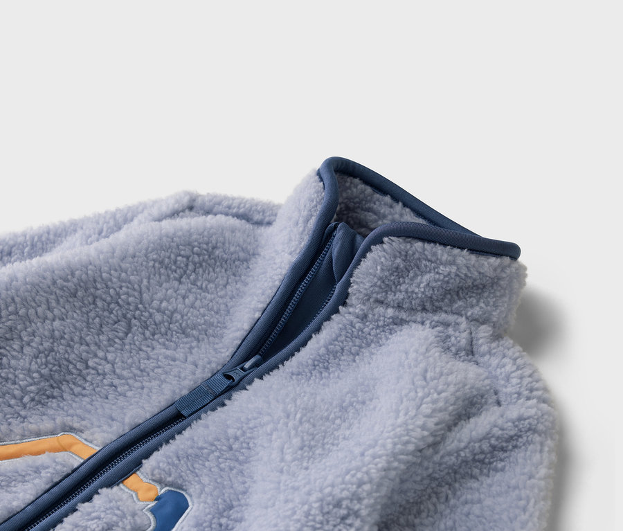 Zbliżenie na jasnoniebieską kurtkę polarową z niebieskim zamkiem błyskawicznym.