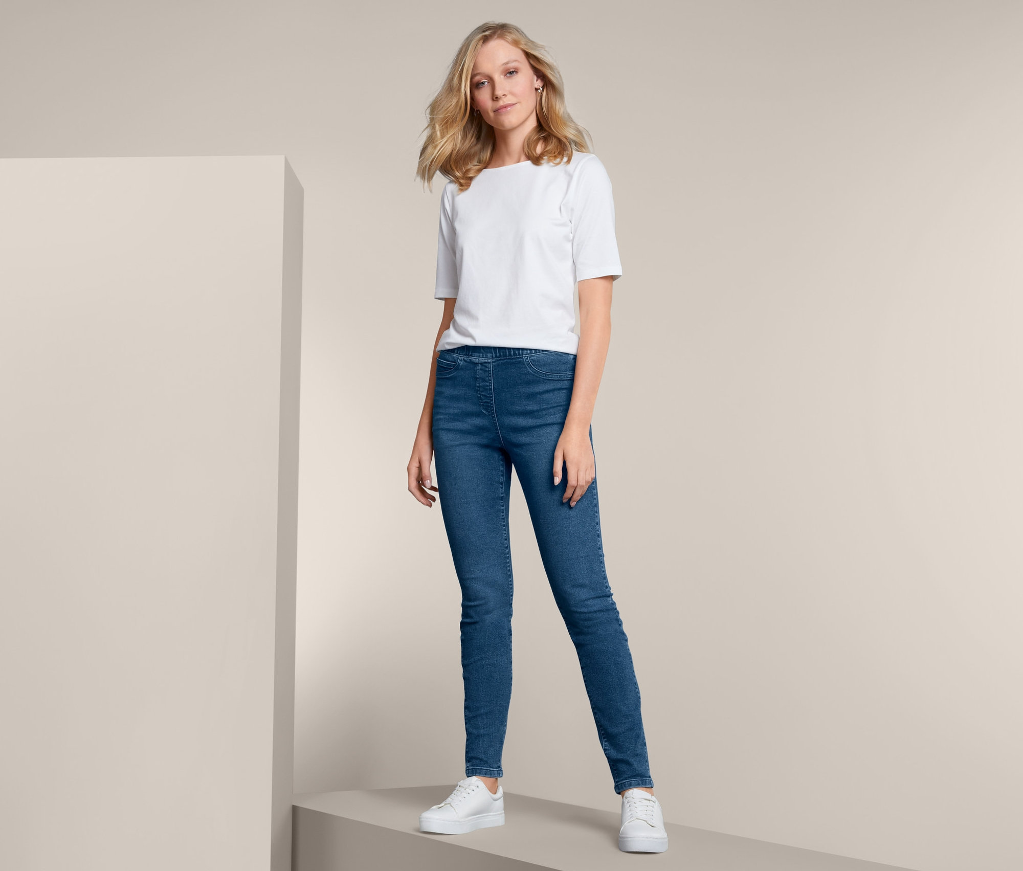 Blondynka pozuje w niebieskich tregginsach i białym T-shircie.