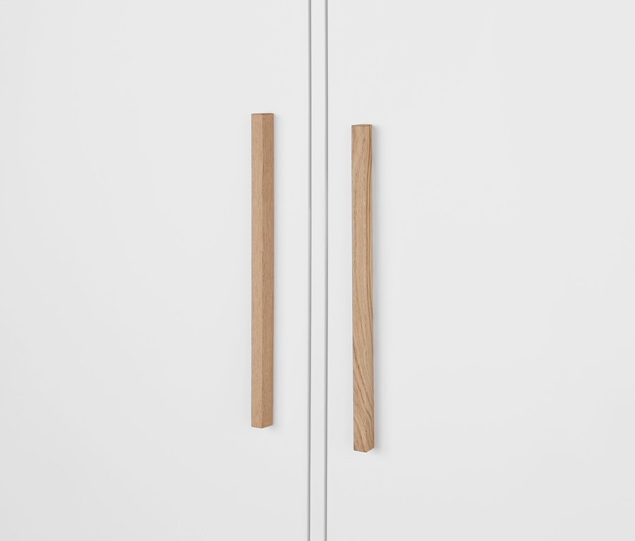 Fragment białej szafy na ubrania »Eklund« z szufladami, ukazujący drewniane uchwyty.