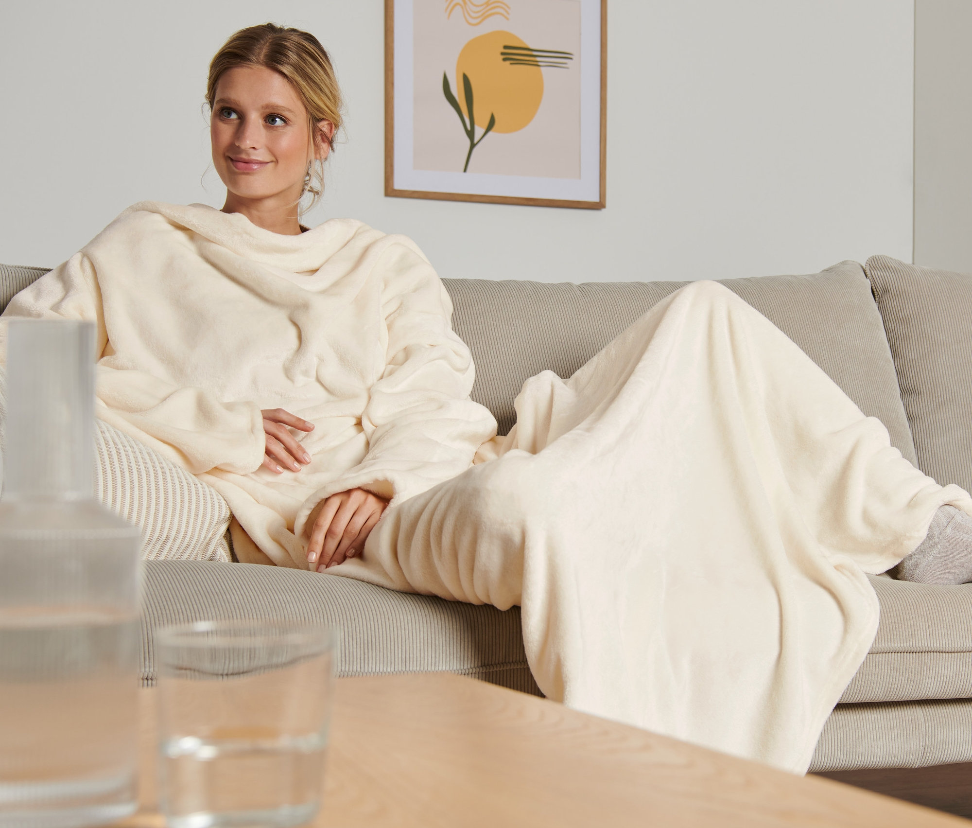 Kobieta siedzi na kanapie i ma na sobie koc z rękawami.