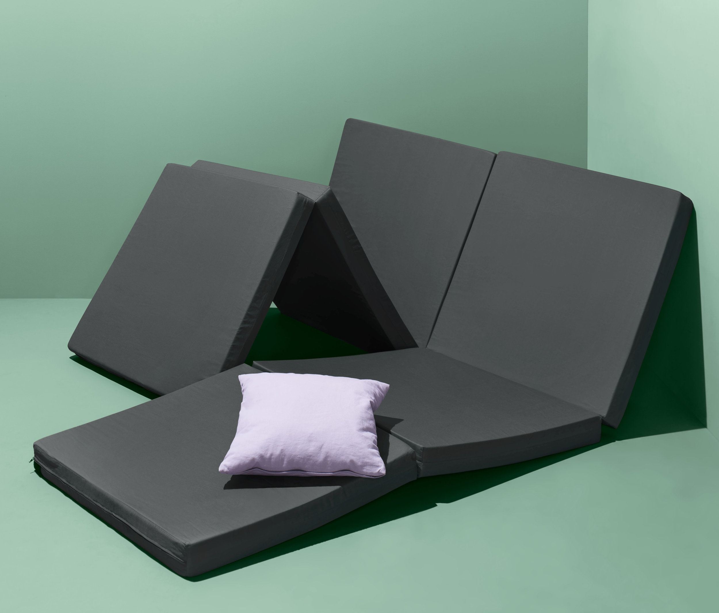 Rozłożony składany materac dla gości z fioletową poduszką na zielonym tle.