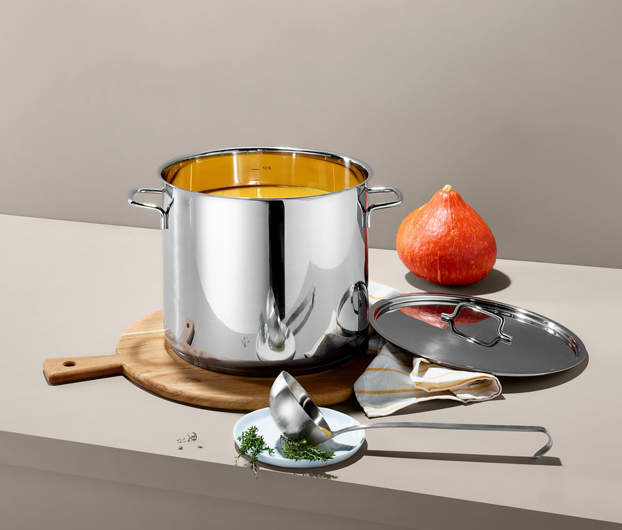 Garnek ze stali nierdzewnej XL stoi na drewnianej desce obok dyni. Pokrywka i chochla leżą obok garnka.