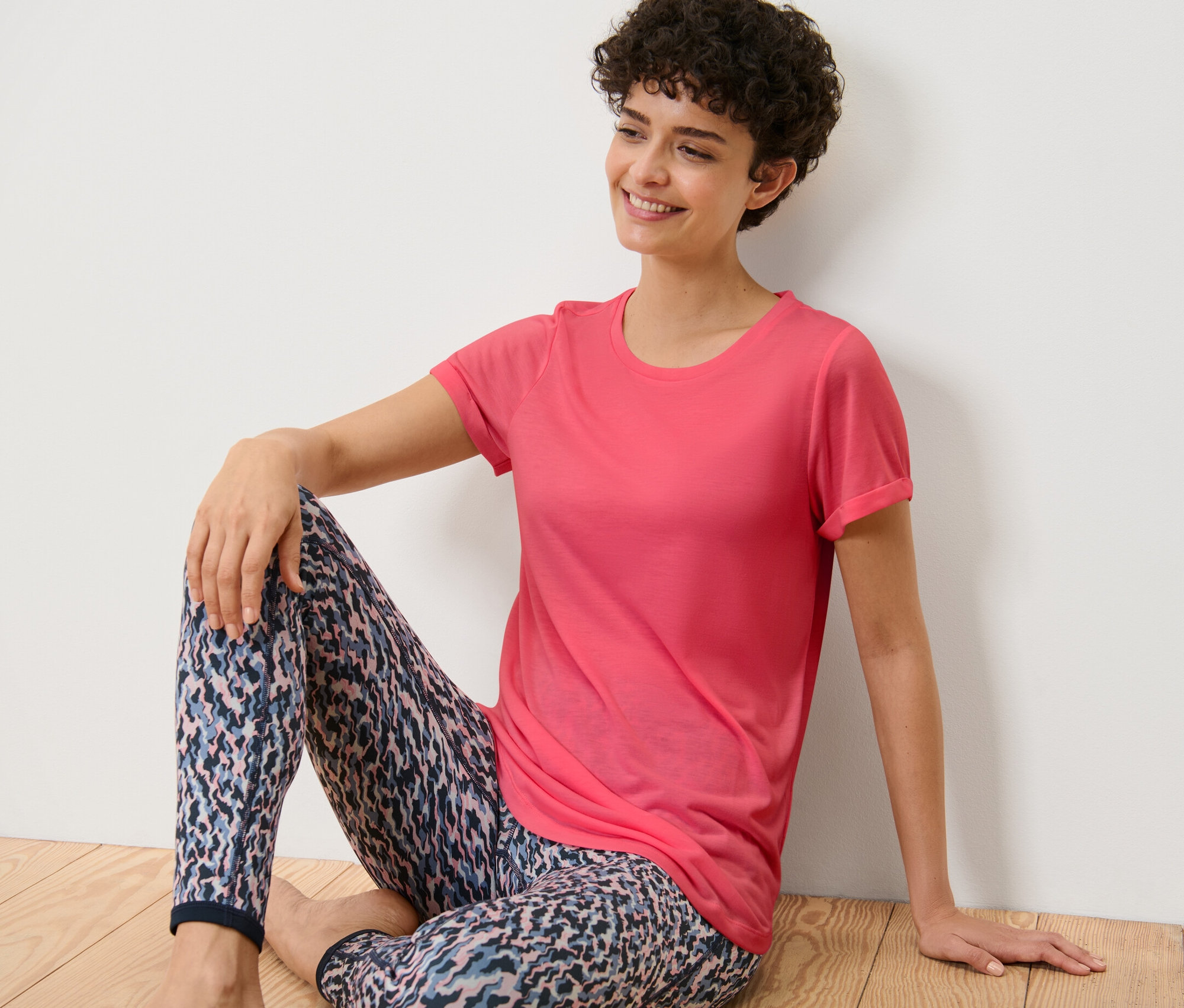 Kobieta siedzi na podłodze w różowej długiej koszulce.