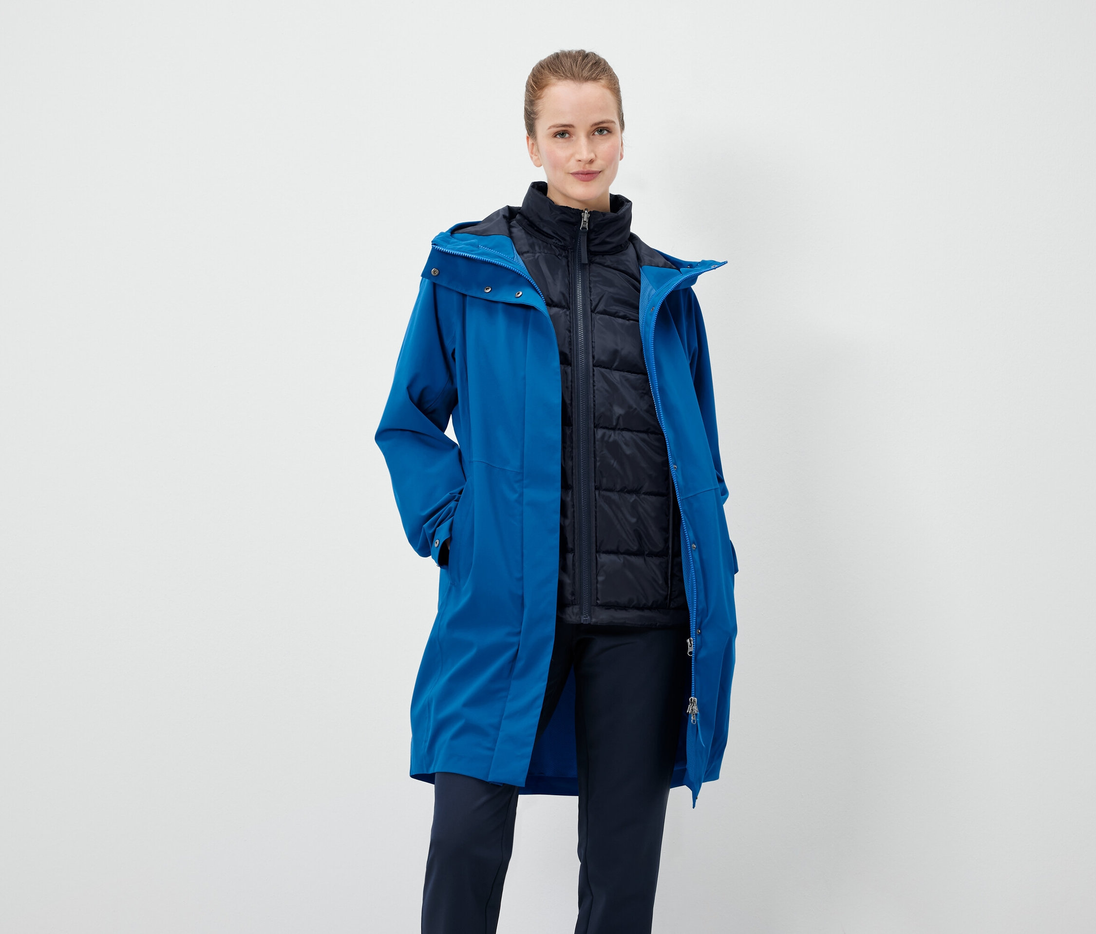 Kobieta ma na sobie niebieski płaszcz i czarną kamizelkę.