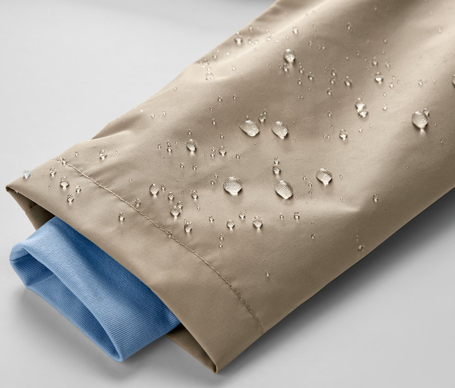 Zbliżenie na brązową kurtkę przeciwdeszczową dla dzieci z kroplami wody i niebieskim rękawem koszuli.