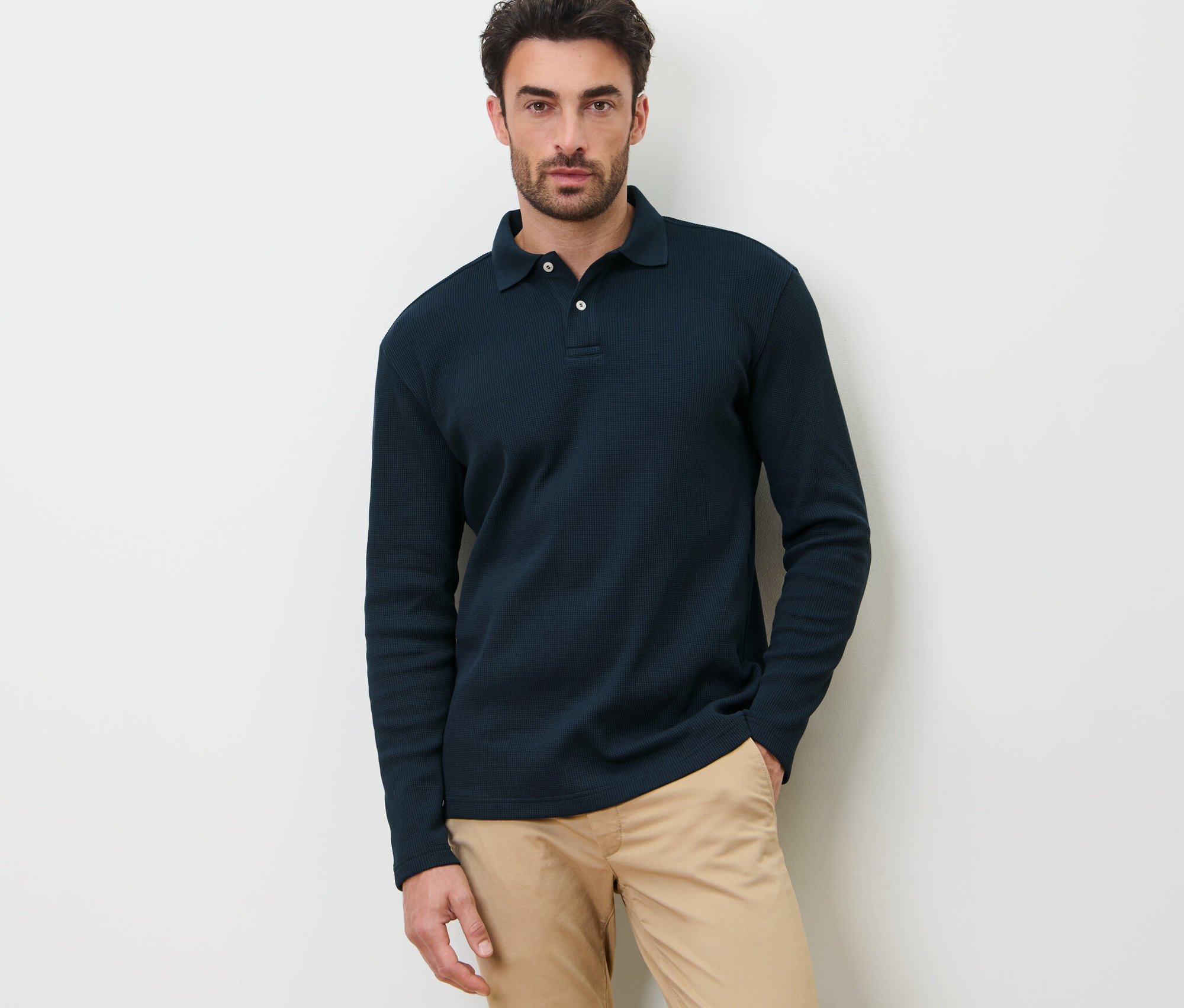 Mężczyzna pozuje na białym tle w granatowej koszulce polo z długim rękawem.