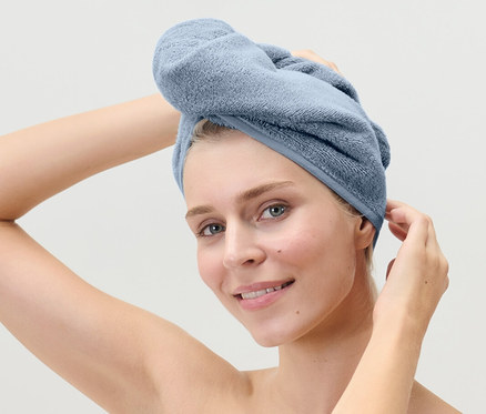 Kobieta poprawia jasnoniebieski ręcznik turban na głowie.