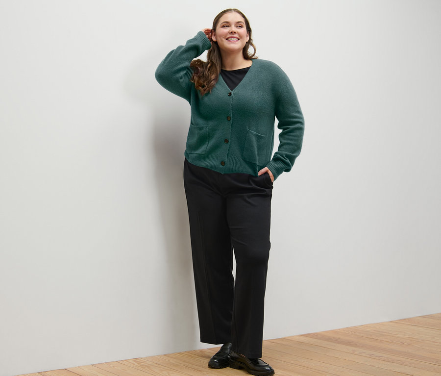 Kobieta pozuje w ciemnozielonym rozpinanym swetrze z zawartością wełny i wygodnych spodniach z dżerseju.