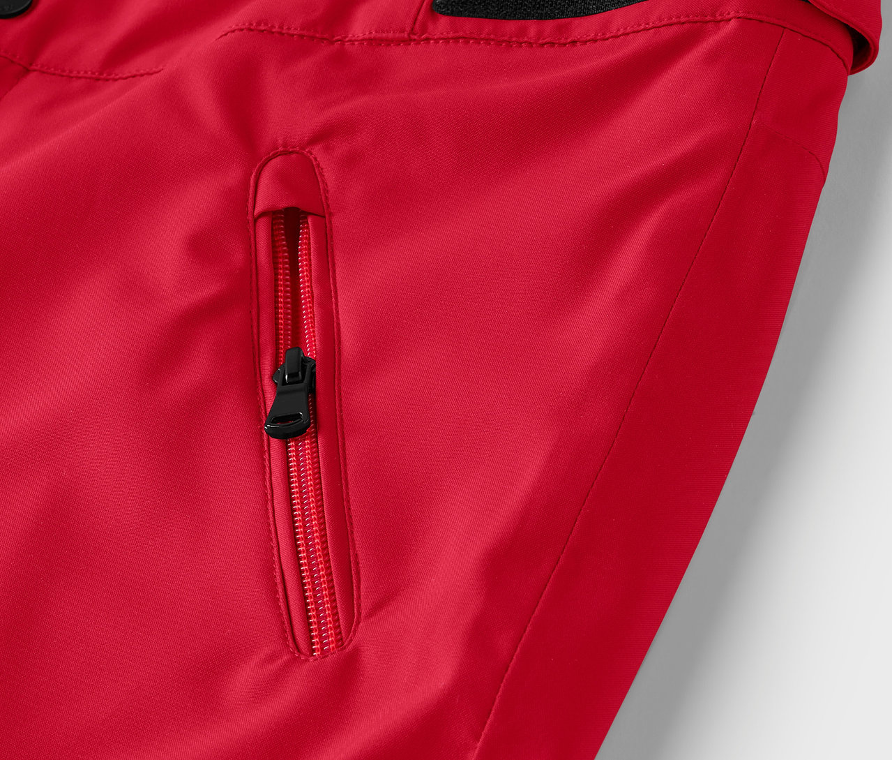 Fragment czerwonej kurtki z czarnym zamkiem błyskawicznym przy kieszeni.