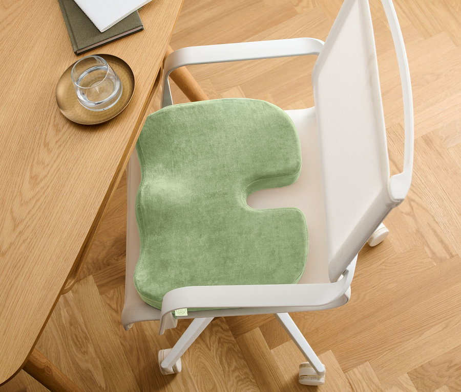 Zielona poduszka do siedzenia z wycięciem w kształcie litery U na krześle. Krzesło stoi przy drewnianym stole.