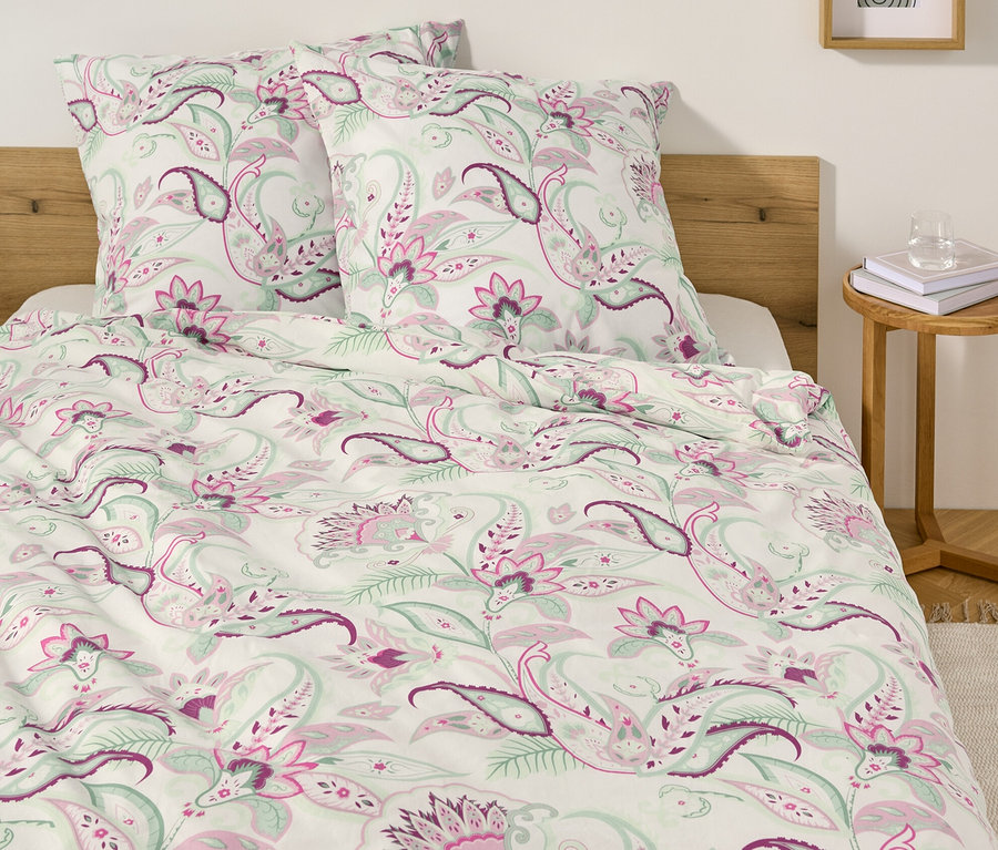 Łóżko z białą pościelą renforcé we wzór paisley i dwiema poduszkami.