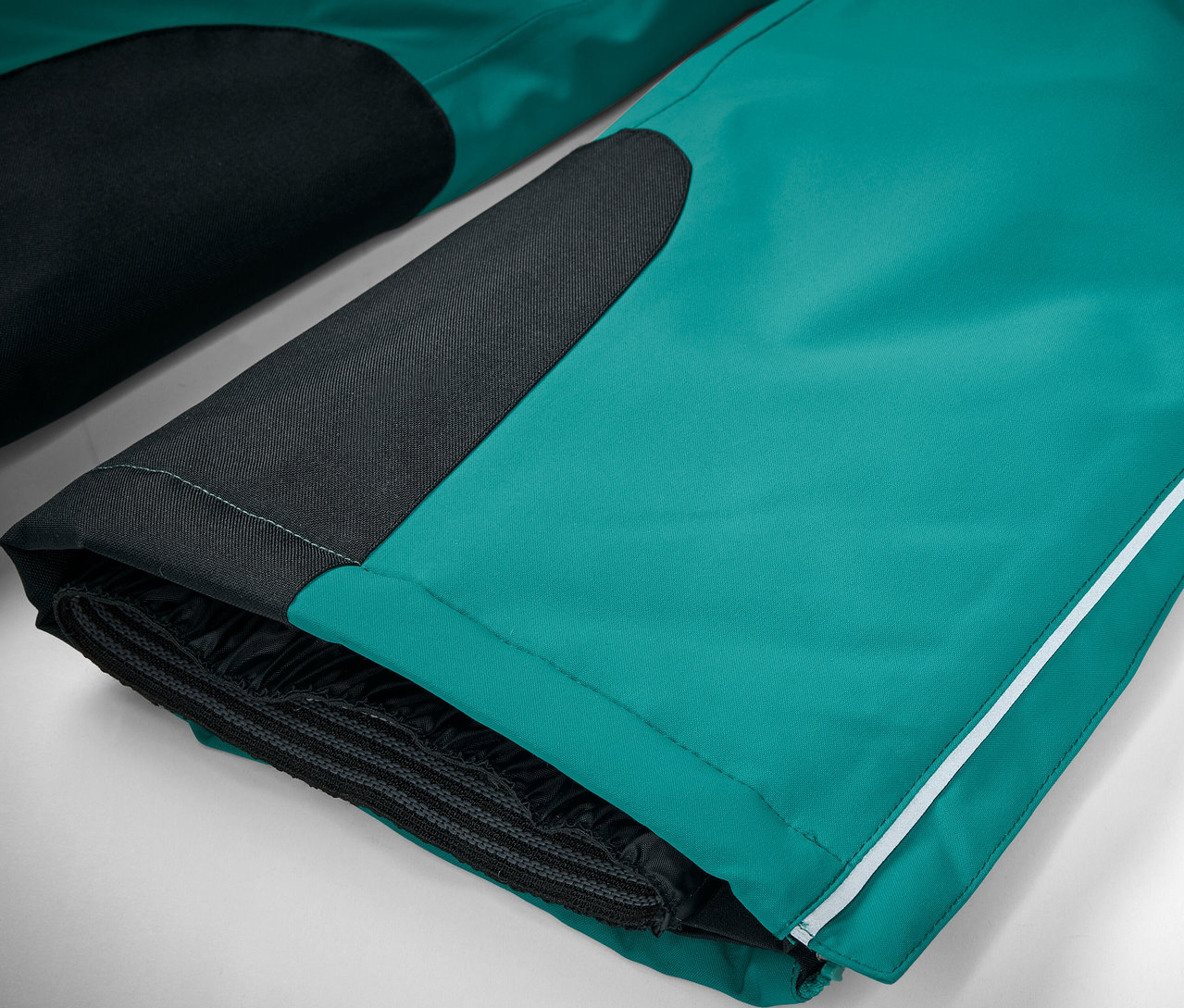 Szczegółowe ujęcie szmaragdowozielonych spodni narciarskich z czarnymi detalami i białym paskiem.