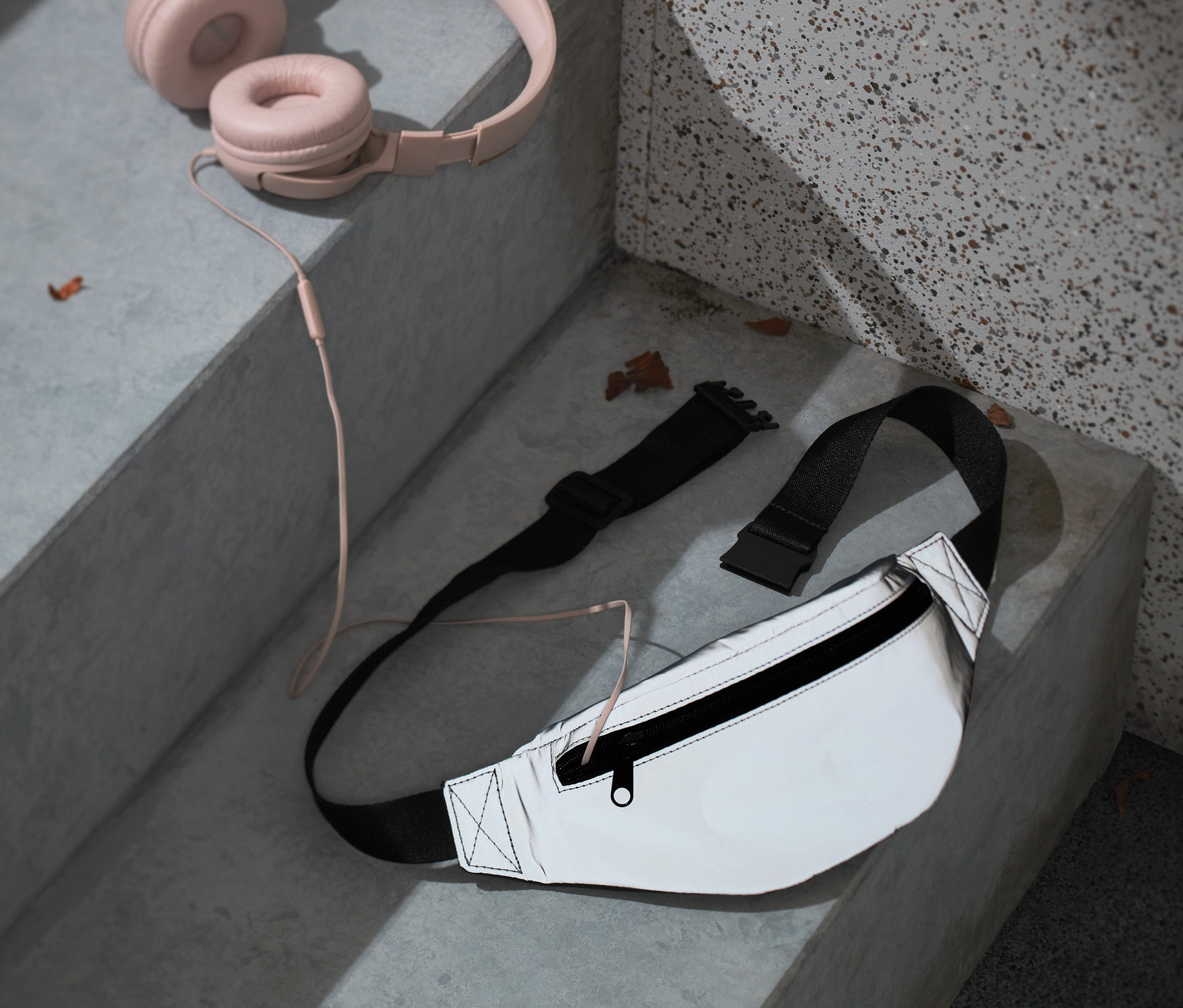 Na schodach leżą różowe słuchawki i nerka z materiału z recyklingu.