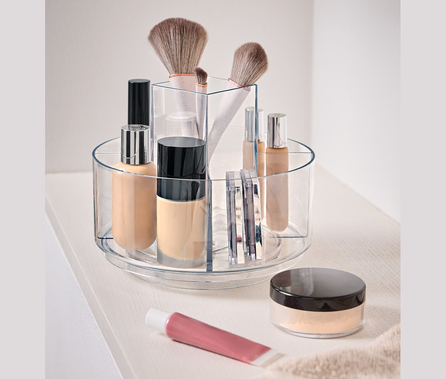 Przezroczysty, obrotowy pojemnik z kosmetykami na białej powierzchni.