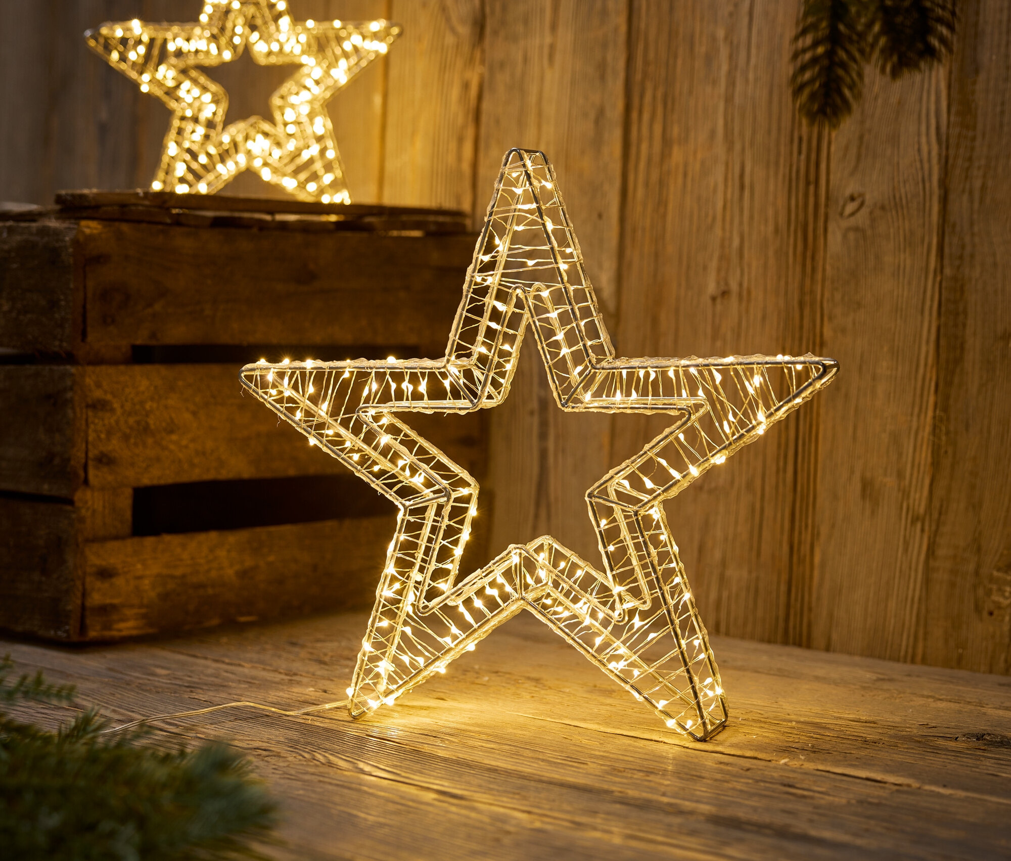 Dwie dekoracyjne gwiazdy z lampkami LED stoją na drewnianej powierzchni.