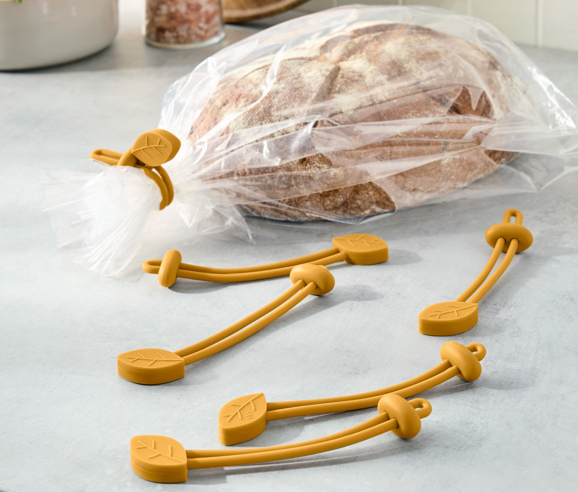 Chleb w plastikowej torbie jest zamknięty żółtą gumką z motywem liścia. Obok leżą trzy inne gumki.