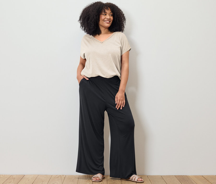Kobieta pozuje w kremowobiałej bluzce z mieszanki modalu i czarnych spodniach palazzo.