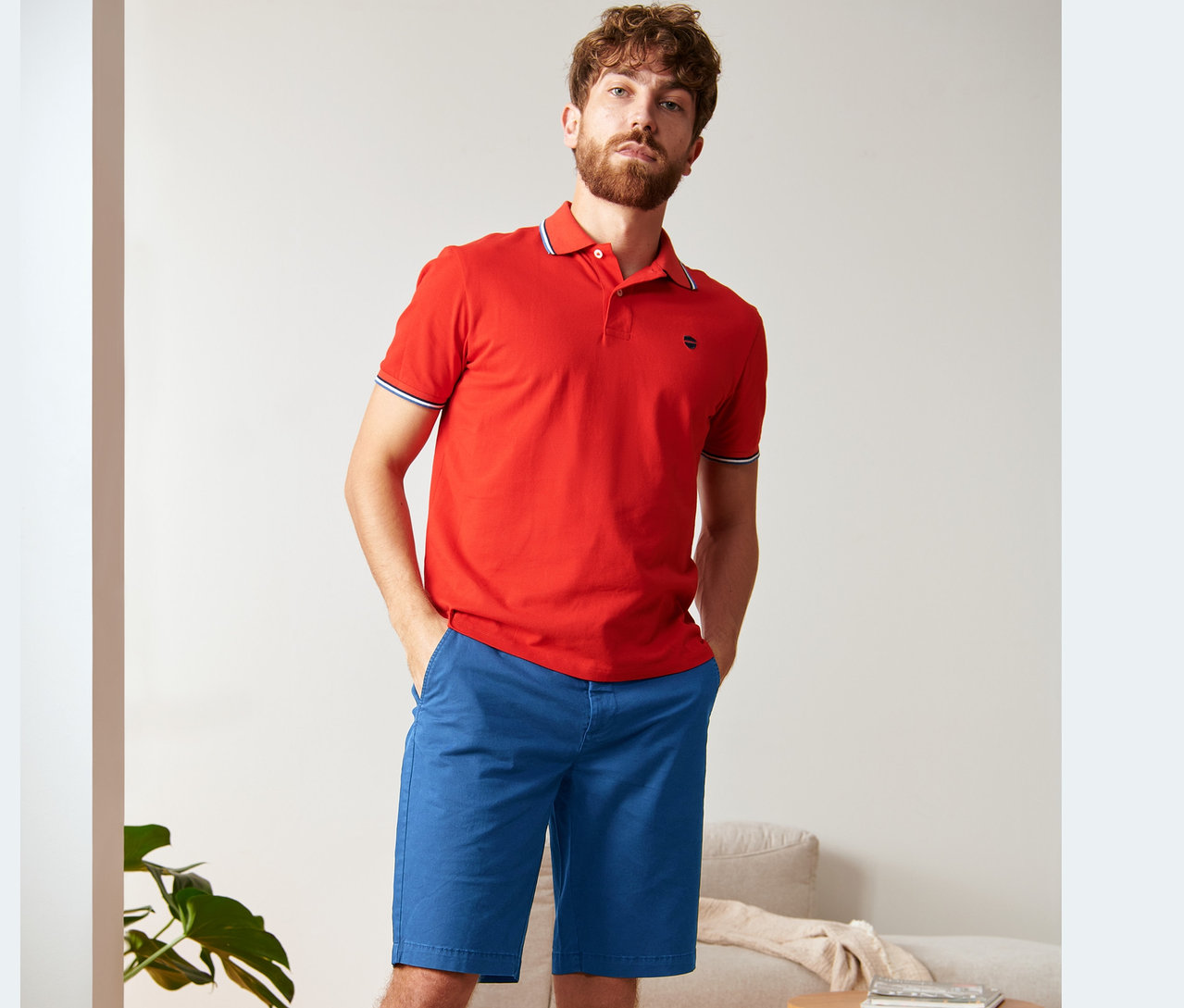 Mężczyzna pozuje w czerwonej koszulce polo i niebieskich szortach chino.