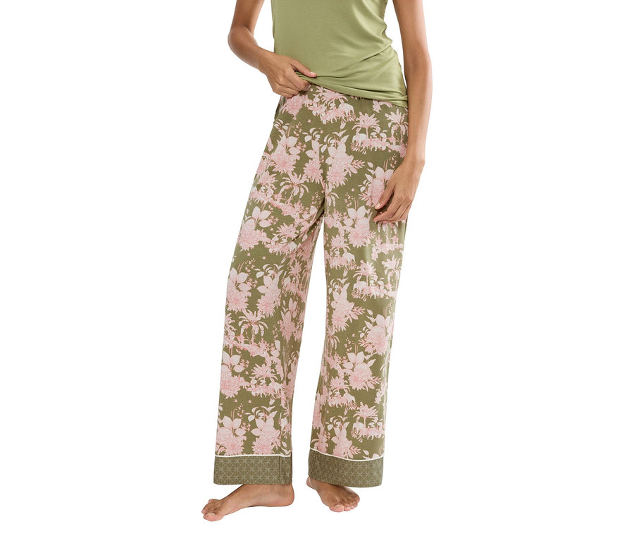 Kobieta ma na sobie zielony top na ramiączkach i oliwkowozielone spodnie od piżamy w różowe kwiaty.