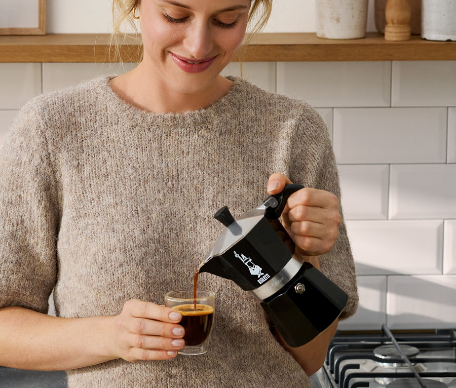 Kobieta nalewa kawę z czarnej kawiarki Bialetti Moka Express, 190 ml, do filiżanki.