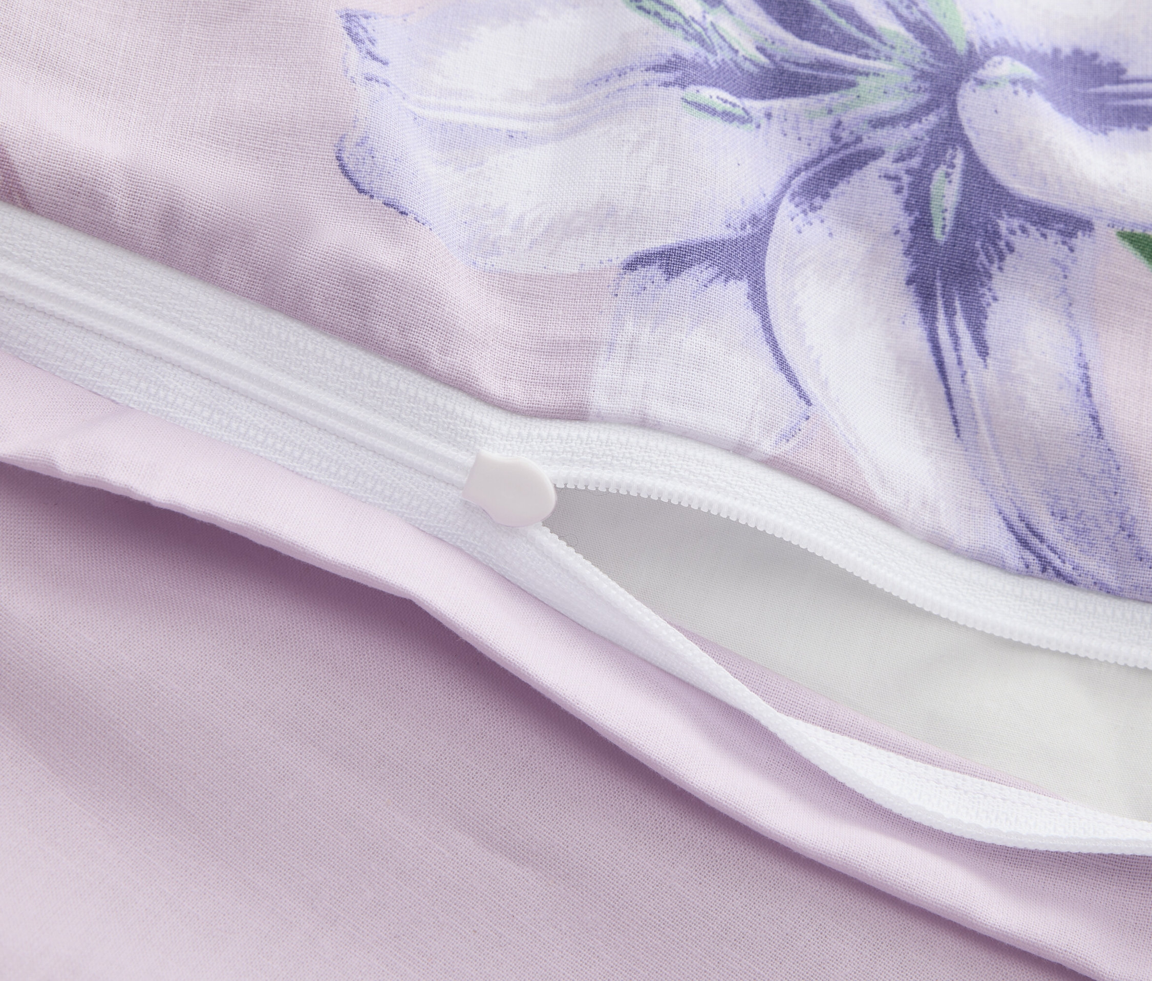 Zbliżenie częściowo otwartej fioletowej poszwy na kołdrę z kwiatowym nadrukiem i zamkiem błyskawicznym.