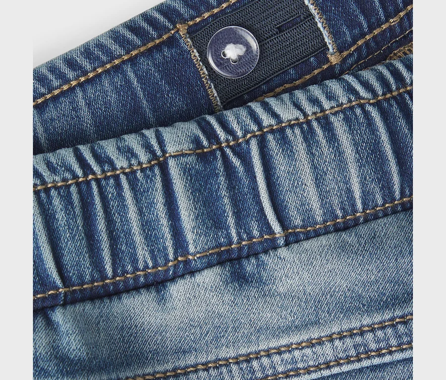 Zbliżenie na niebieskie dżinsy NAME IT Slim Sweat Jeans, ukazujące elastyczny pas z przezroczystym guzikiem do regulacji i brązowe szwy.
