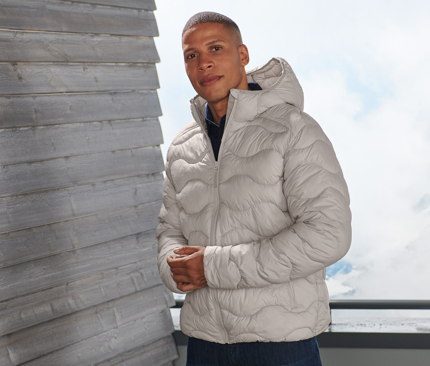 Mężczyzna pozuje na balkonie w beżowej kurtce pikowanej.