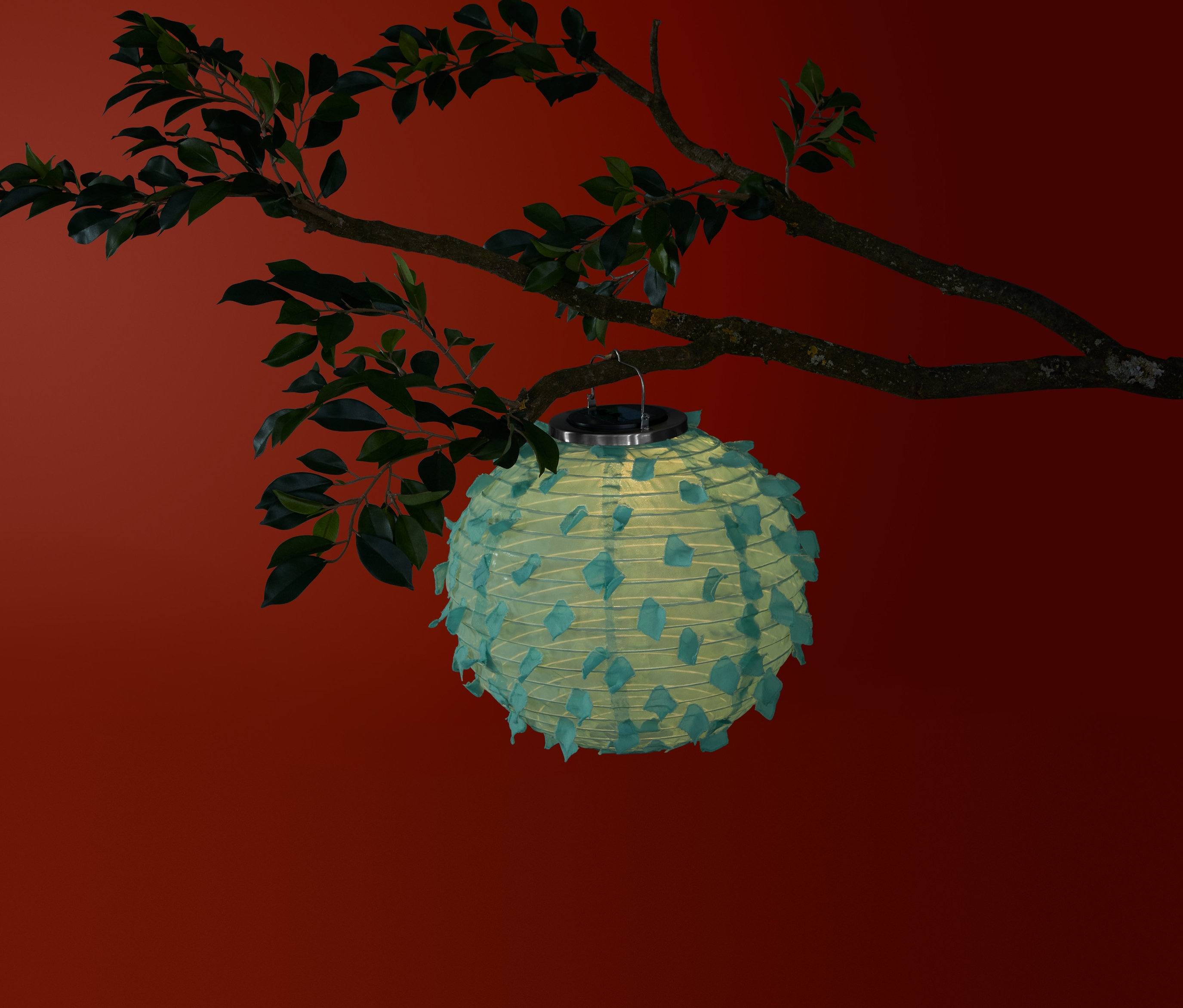 Zielony lampion solarny, kula, zwisa z gałęzi drzewa na czerwonym tle.