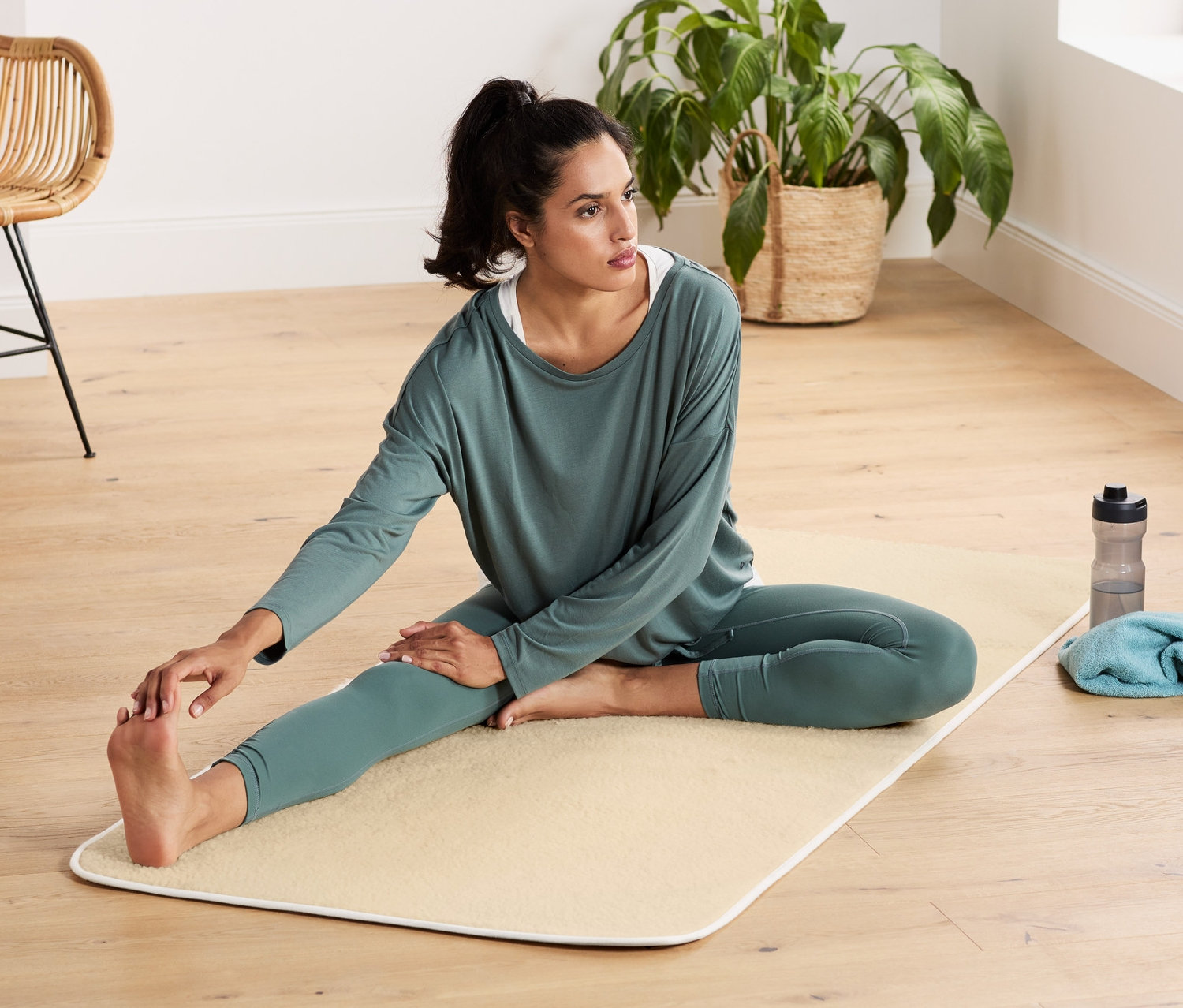 Kobieta rozciąga się na macie do jogi z żywej wełny.