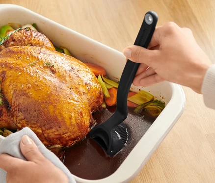 Ręce smarują pieczonego kurczaka w naczyniu do pieczenia pędzelkiem do ciasta i pieczeni.