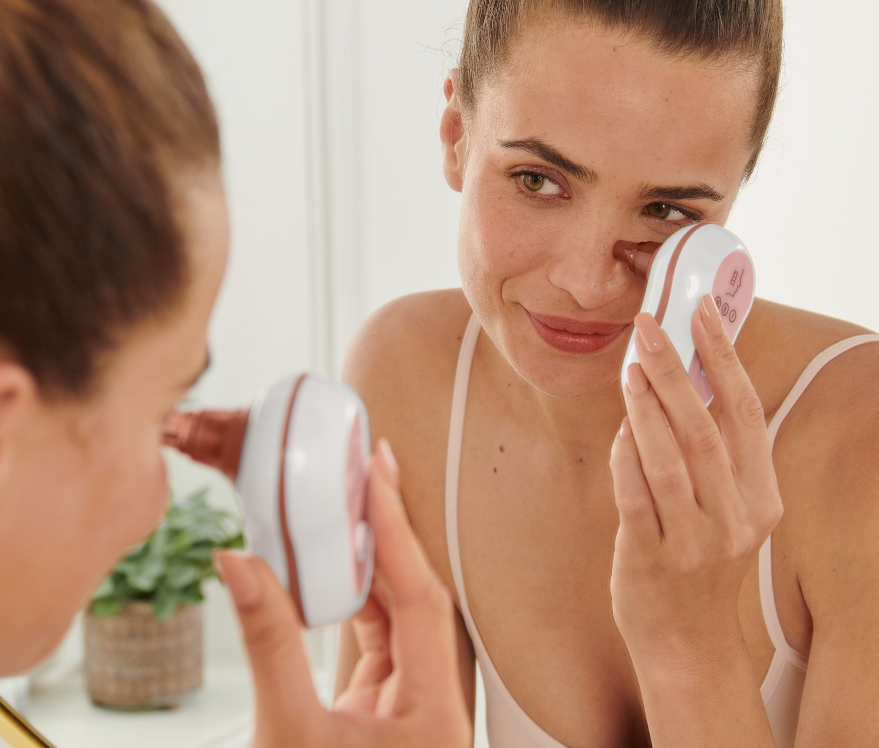Kobieta używa urządzenia do oczyszczania porów na twarzy przed lustrem.