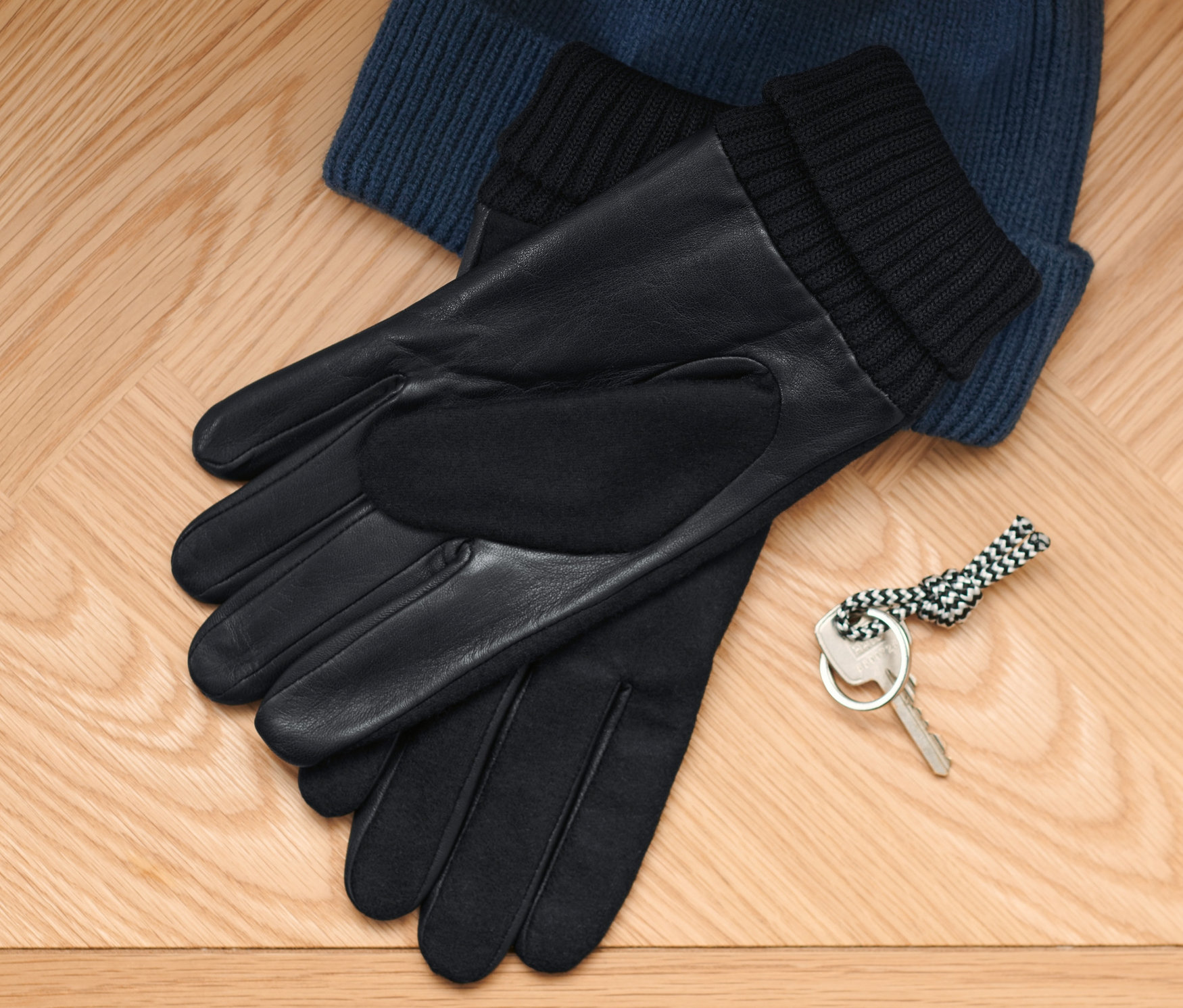 Na drewnianej podłodze leżą niebieska czapka z dzianiny, rękawiczki skórzane i klucz.