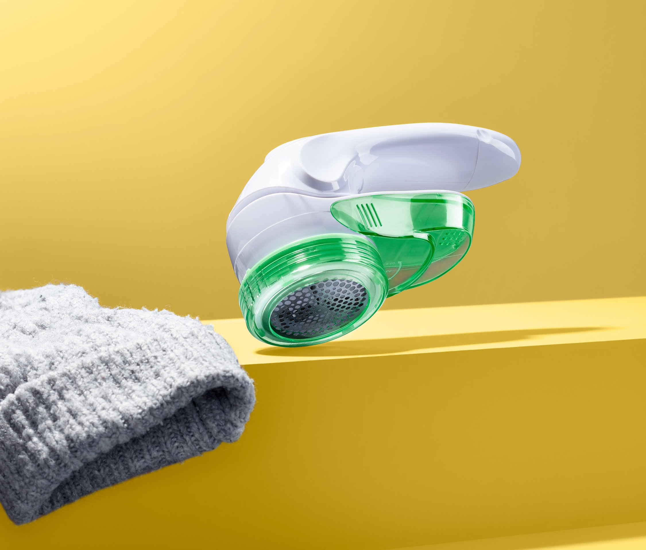 Golarka do zmechaceń z obrotową głowicą leży obok szarej czapki na żółtym tle.