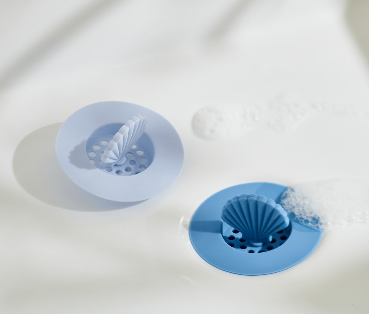 Dwa silikonowe sitka do odpływu w zlewie. Jedno jasnoniebieskie, drugie niebieskie.