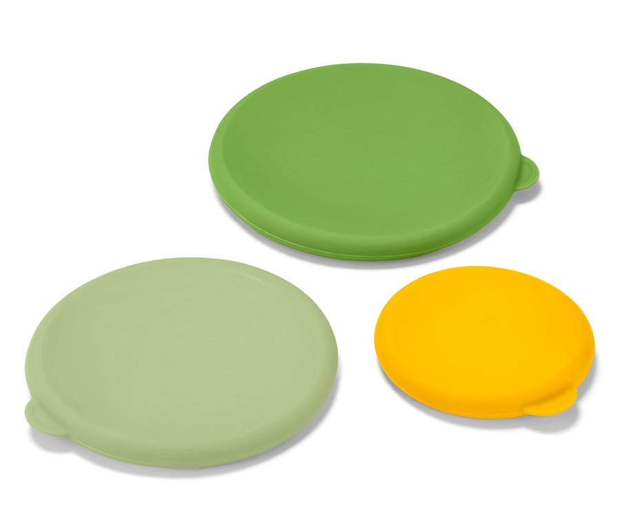 Trzy silikonowe pokrywki: zielona, jasnozielona i żółta, leżą na białej powierzchni.