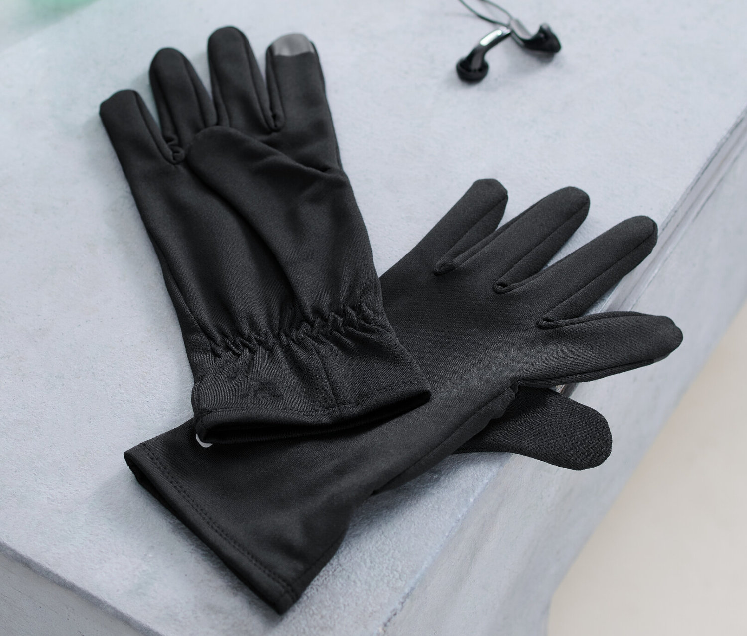 Na ławce leżą rękawiczki do biegania, butelka z wodą i słuchawki.