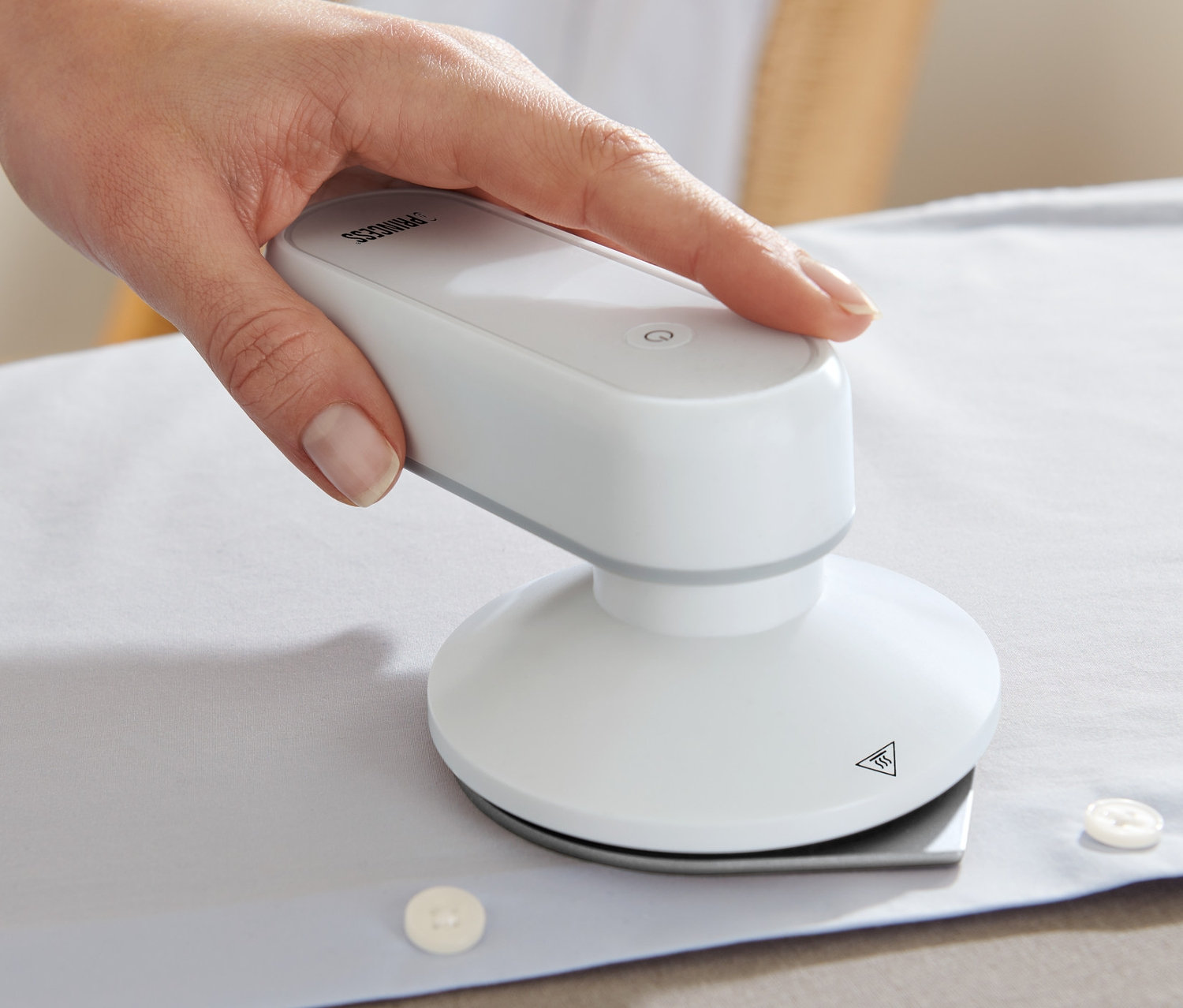 Ręka prasuje białą koszulę żelazkiem podróżnym Princess z powerbankiem.