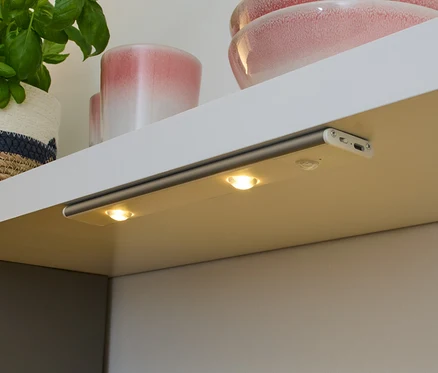 Bezprzewodowa wielofunkcyjna lampka LED zamontowana pod półką oświetla blat.